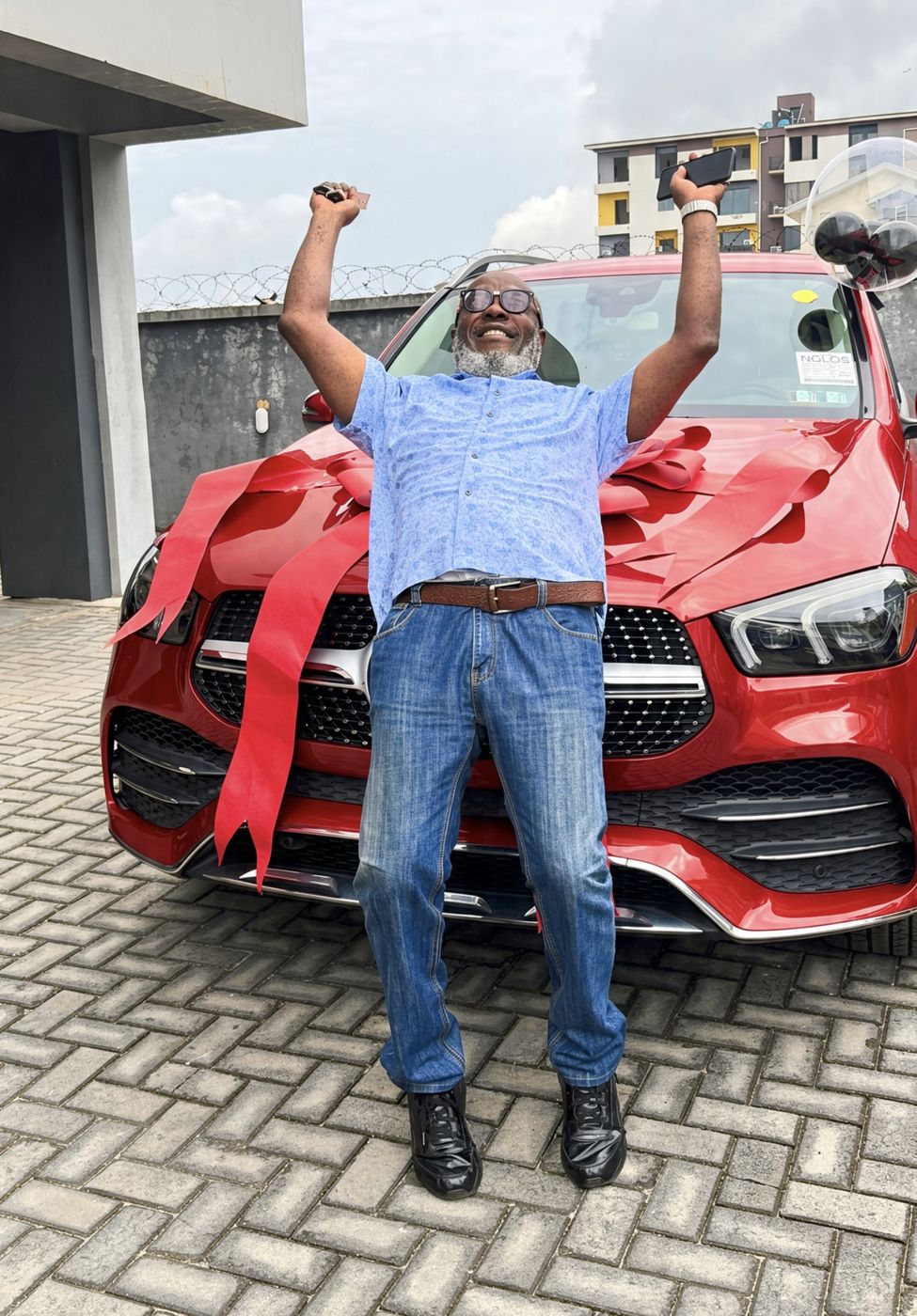Man celebrating with arms raised in front of a ribbon-wrapped Mercedes-Benz