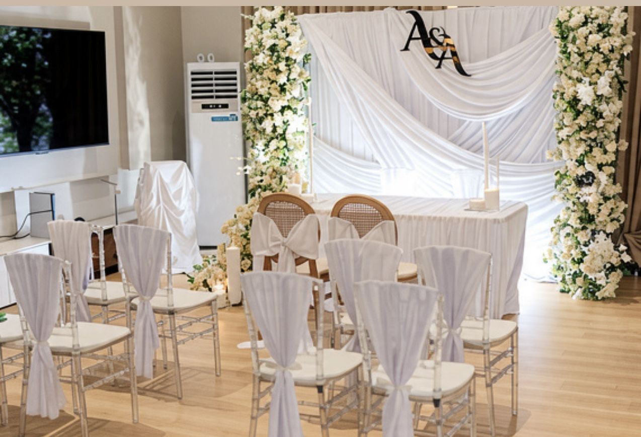 White-draped wedding ceremony backdrop with floral pillars and monogrammed signage